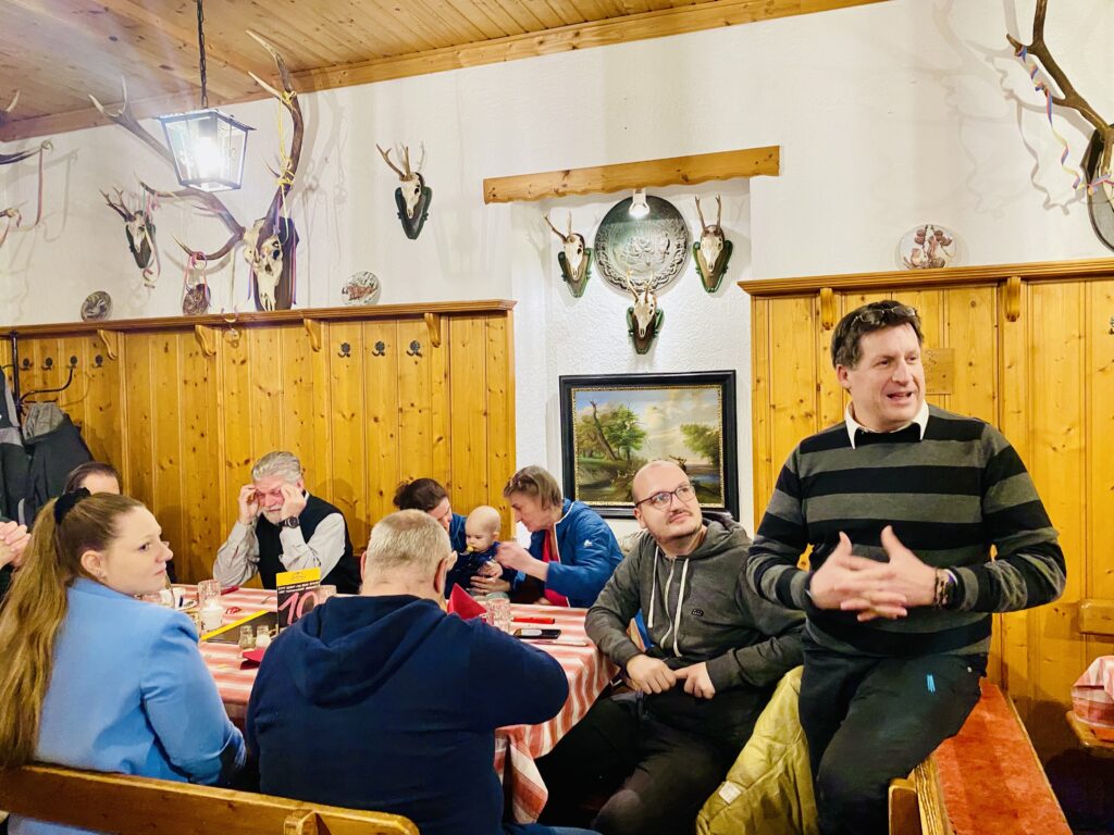 Michael Schmid, Obmann des Samariterbund Ottakring, hält seine Festrede. Im Hintergrund sitzt ein Teil des ehrenamtlichen Teams des Samariterbund ottakring zu Tisch.