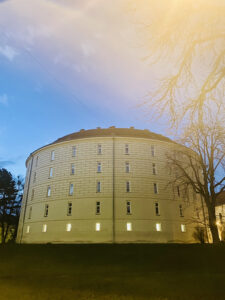 Die Außenfassade des Narrenturms in der Dämmerung. Ein rundes, fünfstöckiges, weißes Gebäude.